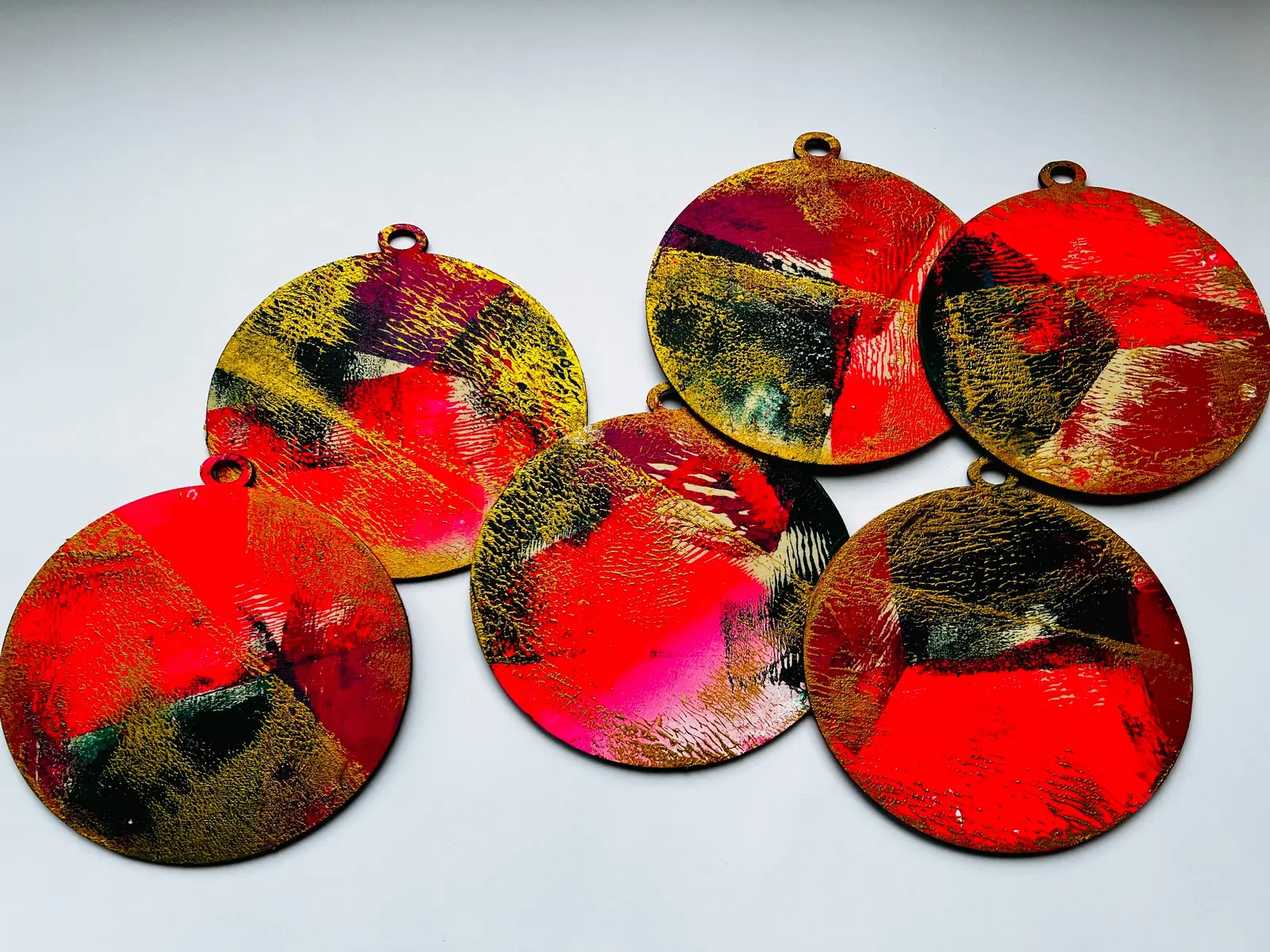 Rounded gelli printed hanging forms layered in red, gold, black and pink.