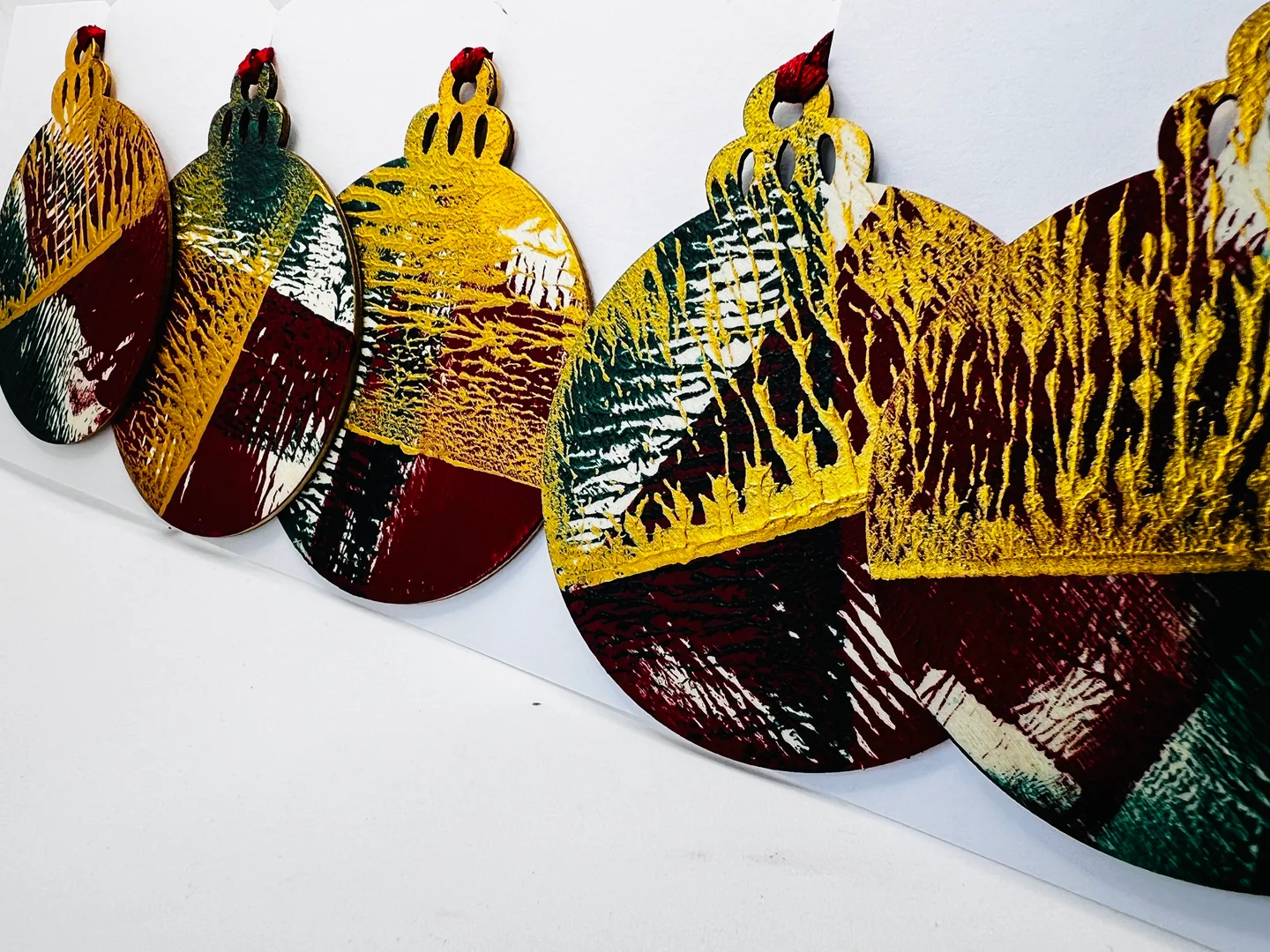 Group of rounded hanging forms in ochre, burgundy, green, black and white, arranged in a shallow row.