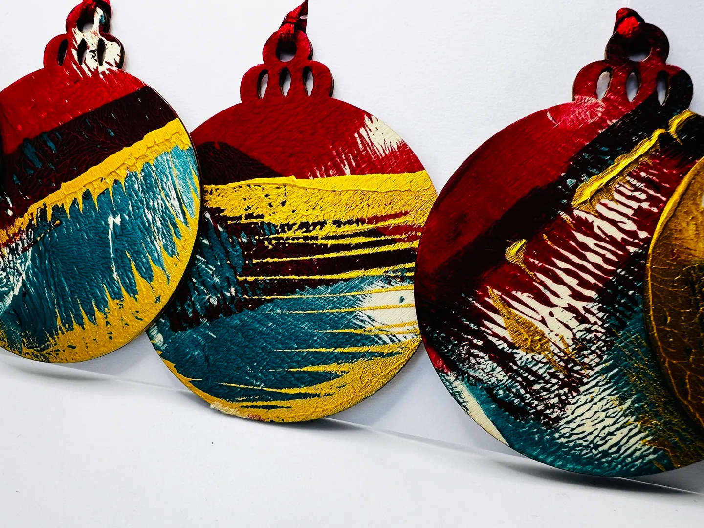 Close view of rounded hanging forms with bold teal, ochre, red, black and white painted patterns.