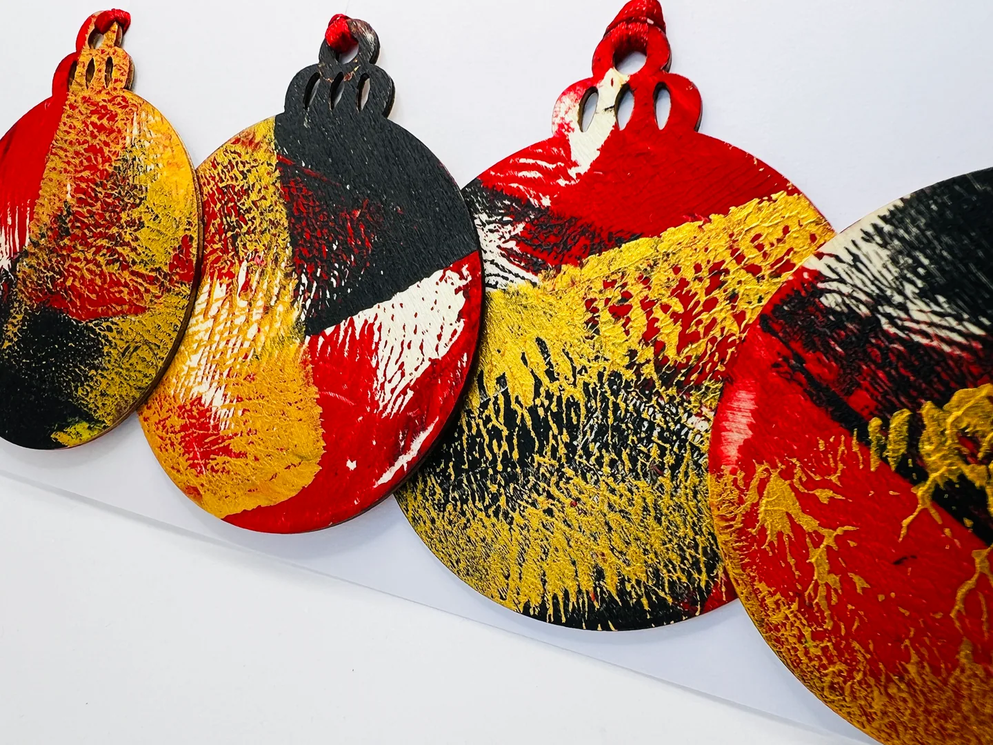Rounded hanging forms with vivid red, ochre, charcoal and white layered patterns against a pale background.