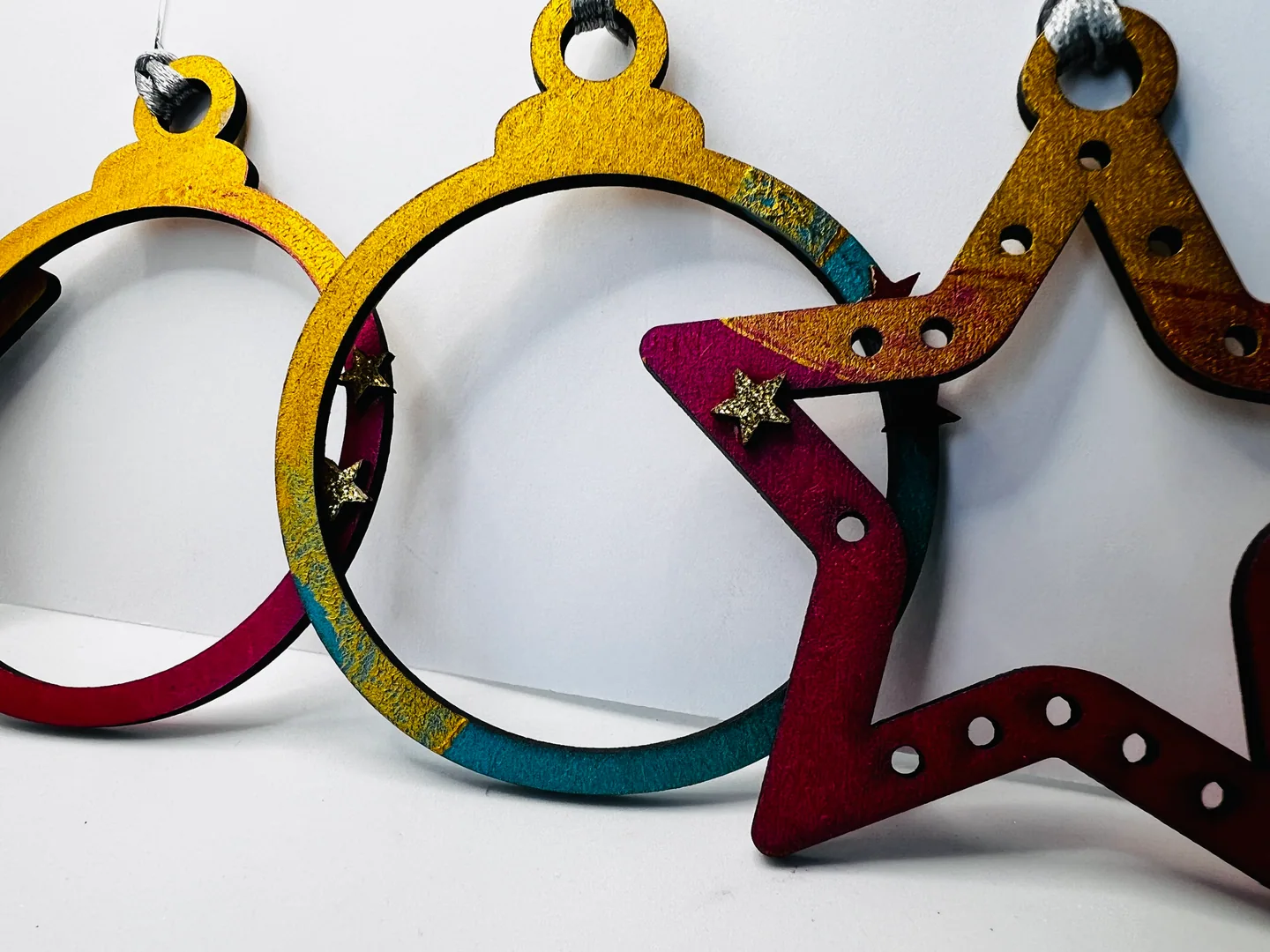 Close view of open circular and star-shaped hanging forms in ochre, teal, magenta and deep red.