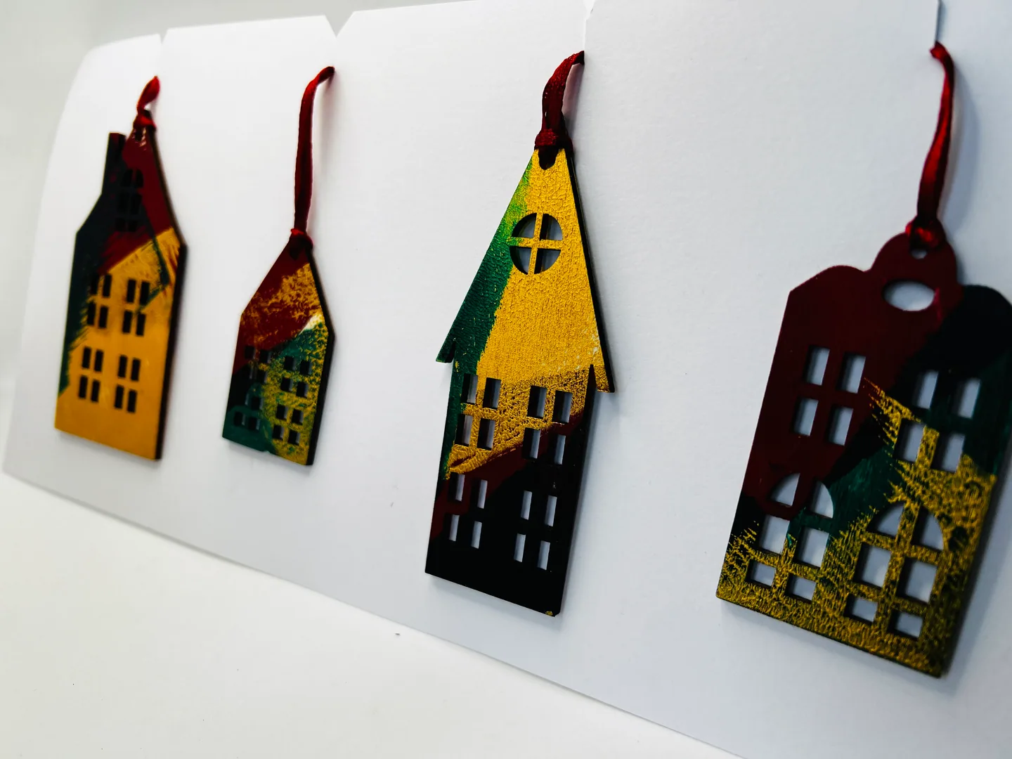 Four narrow house-shaped hanging forms in ochre, green, deep red and black, displayed on white folded panels.